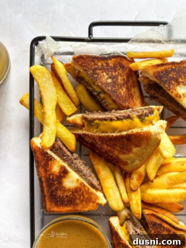 Close up of a Dunker Burger cut in half, revealing juicy beef and melted cheese between Texas Toast, with a small bowl of au jus for dipping.