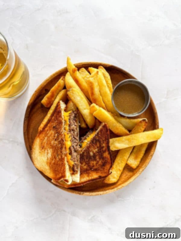 A close-up shot of a Dunker Burger, showing the golden Texas Toast, melted cheese, and juicy beef patty. A small bowl of au jus is next to it.