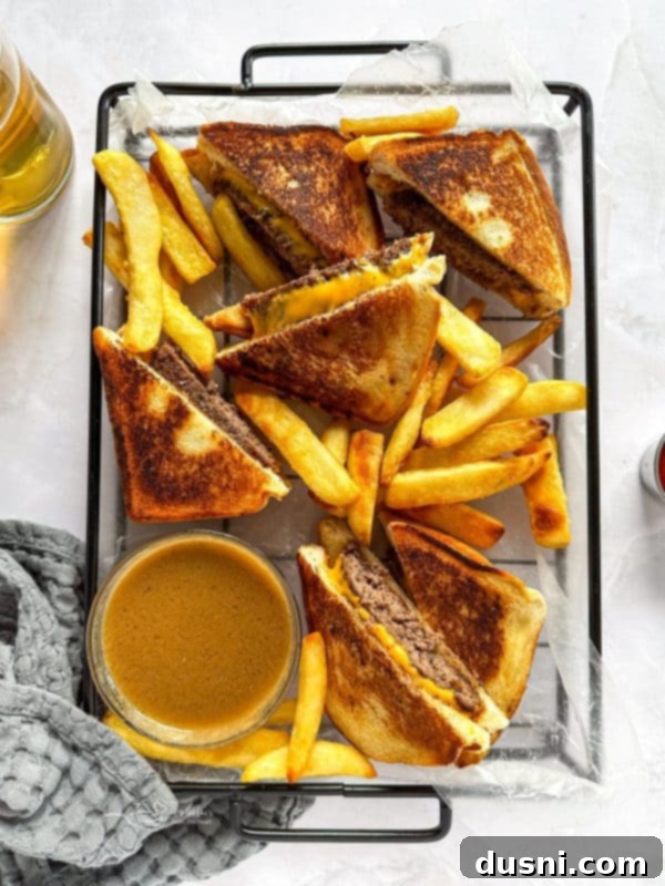 A plate with a Dunker Burger cut in half, alongside a small bowl of au jus for dipping.