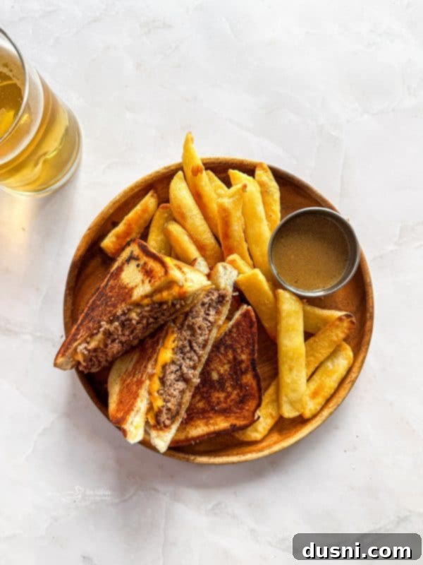 Two Dunker Burgers on a cutting board, one whole and one cut in half, showing the cross-section with beef and melted cheese between Texas Toast. A small ramekin of au jus is placed next to them.