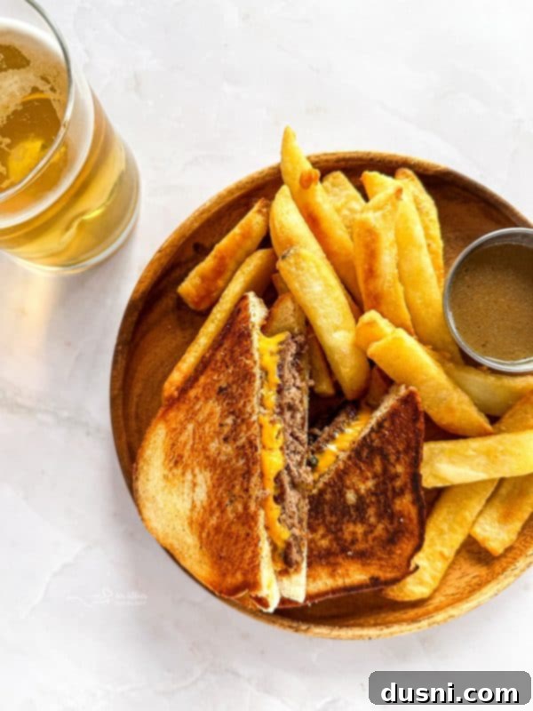 Close up of a Dunker Burger cut in half, revealing juicy beef and melted cheese between Texas Toast, with a small bowl of au jus for dipping.