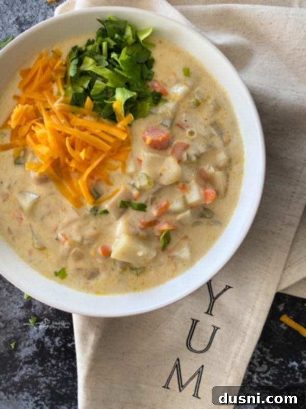 Top view of cheesy potato soup in white bowl with cheese and parsley on top