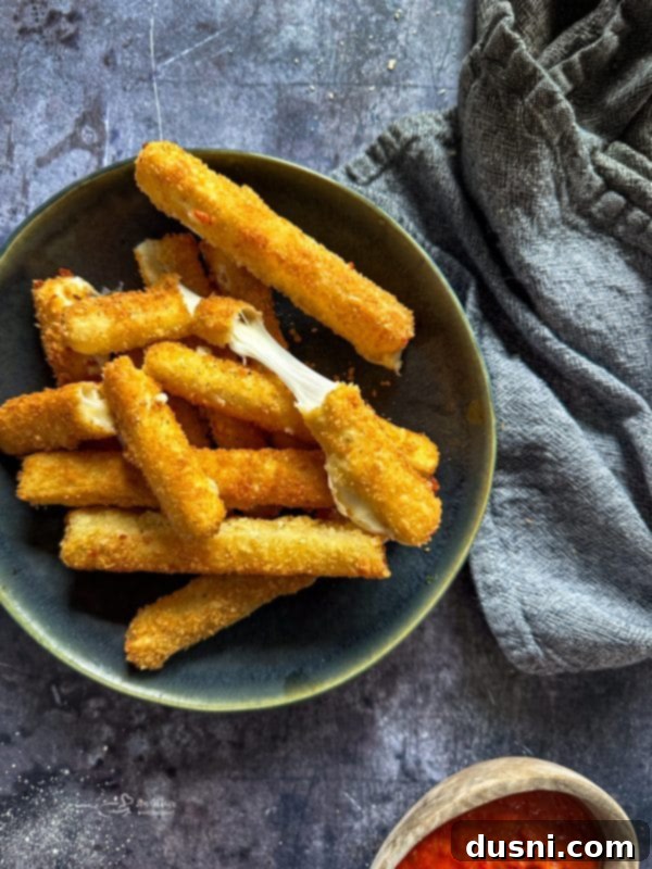Freshly fried homemade mozzarella sticks on a plate, ready to be served with marinara sauce.