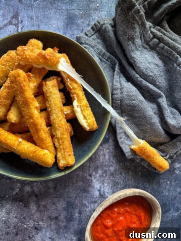 Close-up of a homemade mozzarella stick with a long cheese pull, showcasing its gooey center.