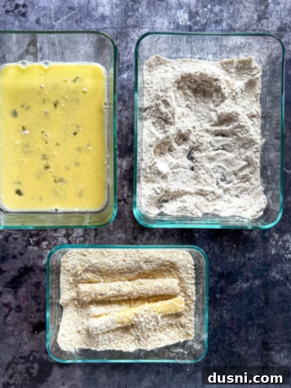 First step of breading: dipping mozzarella stick in egg mixture.