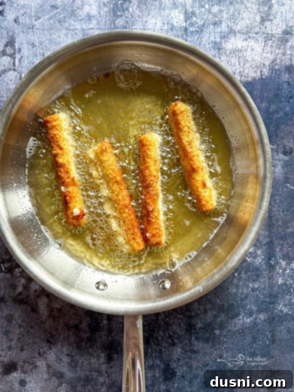 Coated mozzarella sticks arranged on a baking sheet, ready for freezing.