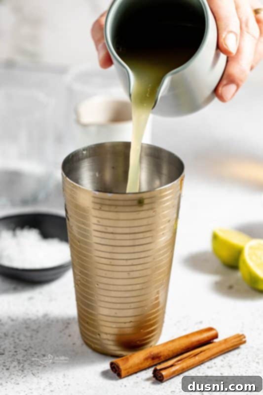 Apple Cider Margarita 9 Ingredients being poured into a cocktail shaker with ice.