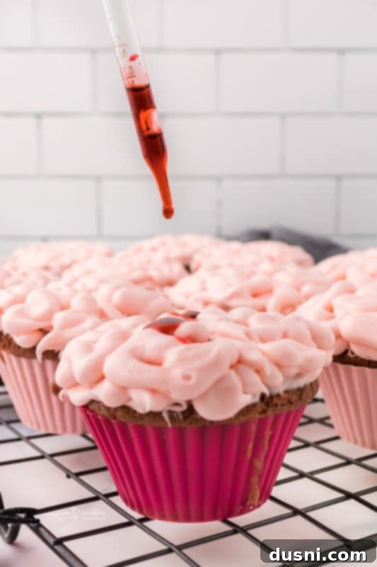 Ghoulish Grey Matter Cupcakes 16 A close-up shot showing the detailed piping technique used to create the brain-like texture on a Halloween cupcake with pink cream cheese frosting, just before the edible blood is added.