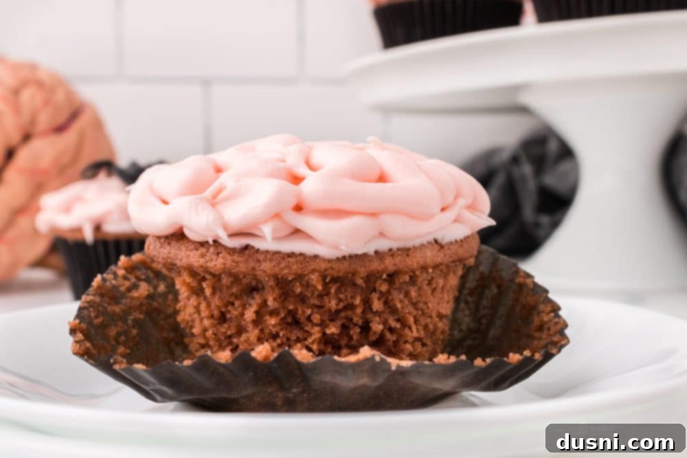 Ghoulish Grey Matter Cupcakes 3 Close-up shot of several Halloween Brain Cupcakes arranged on a dark, rustic wooden surface. The intricate brain-like frosting and shiny edible blood are clearly visible, creating an unsettling yet appetizing visual for a Halloween party or gathering.