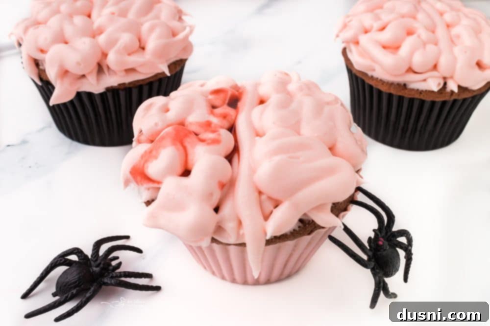 Ghoulish Grey Matter Cupcakes 9 A single Halloween Brain Cupcake displayed prominently on a dark plate, with a background of blurred festive Halloween decorations. The sharp focus on the cupcake showcases the detailed brain frosting and the dripping edible blood, making it an ideal spooky treat.