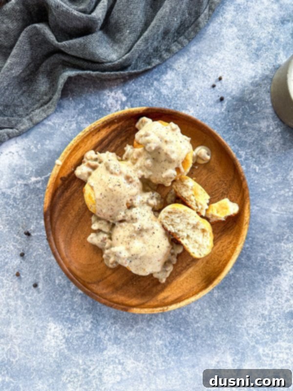 A generous serving of rich, creamy homemade sausage gravy poured over warm, flaky biscuits on a plate.