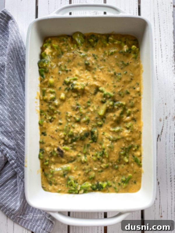 Top view of uncooked broccoli and cheese casserole in white baking dish