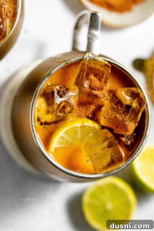 A close-up of a Pumpkin Spice Moscow Mule in a copper mug, garnished with a lime slice and cinnamon stick, on a dark background.