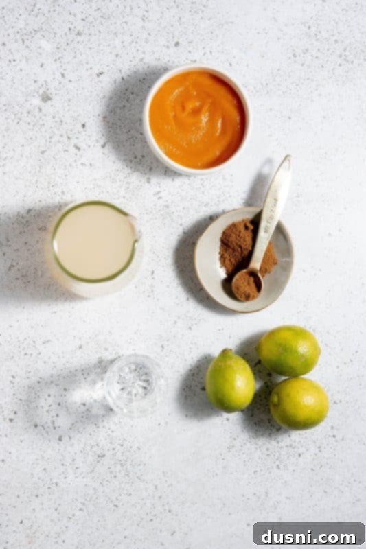Two copper mugs filled with Pumpkin Spice Moscow Mules, garnished with lime and cinnamon sticks, on a wooden surface.