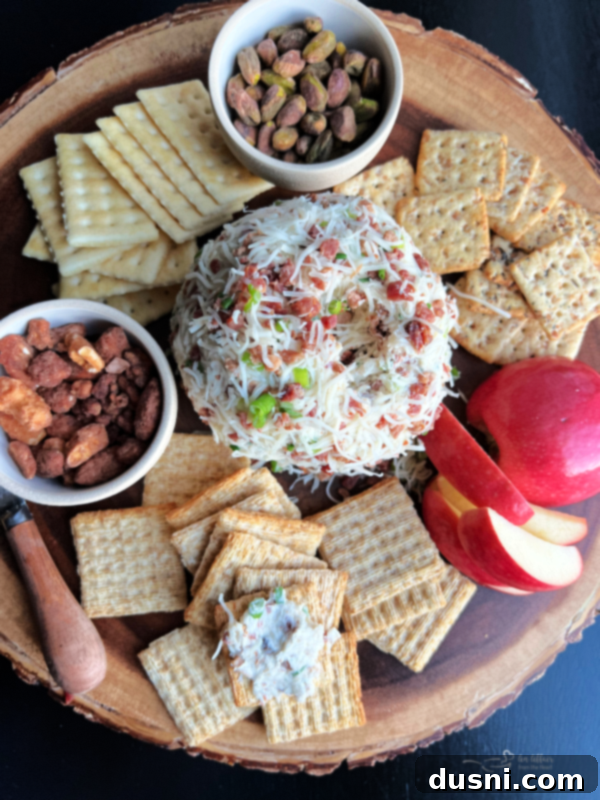 Overhead shot of a beautifully presented Sauerkraut Bacon & Swiss Cheese Ball on a wooden charcuterie board, surrounded by crackers, fresh herbs, and small serving knives.