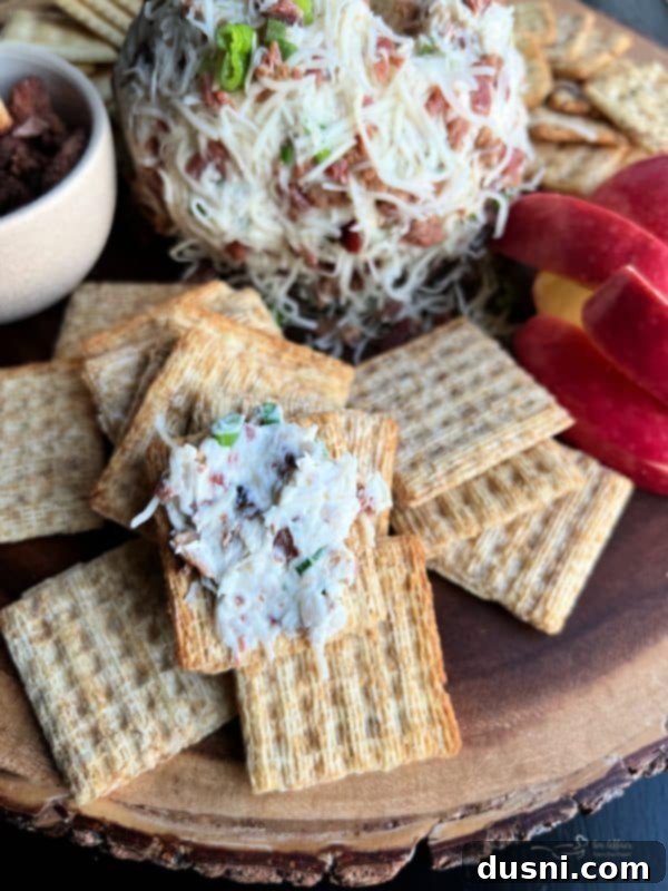Close-up of the Sauerkraut Bacon & Swiss Cheese Ball on a platter, showing the texture of the coating and a cracker with a scoop of the cheese ball.