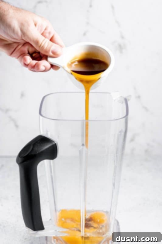 Homemade Blender Eggnog 8 Pouring maple syrup into a blender with eggs, preparing to blend.