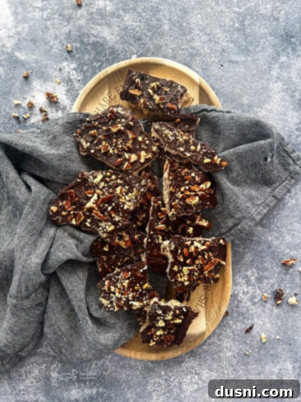 Classic Handcrafted Toffee 11 Three pieces of chocolate-covered toffee with pecans, artfully stacked on a white surface.