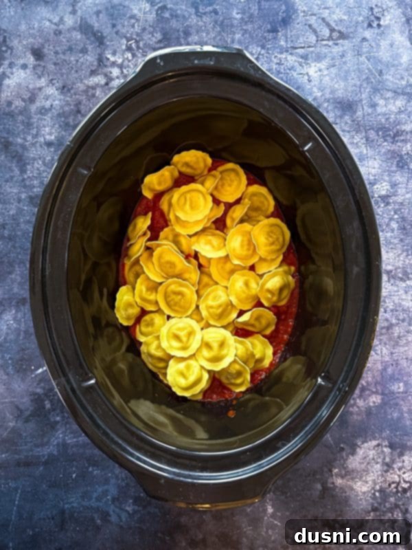Lazy Slow Cooker Ravioli Lasagna 8 Step 3: Spreading half the jarred sauce at the bottom of the slow cooker.