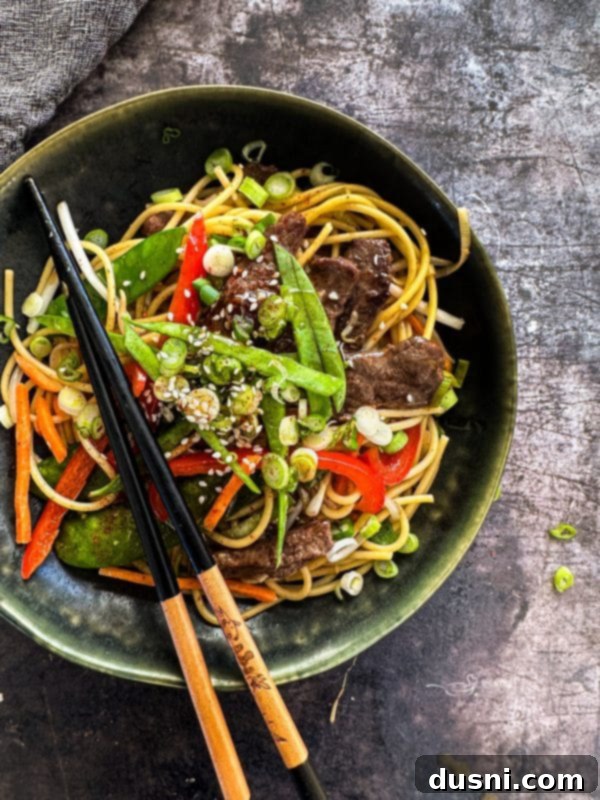 Savory Beef Lo Mein 2 A close-up shot of a bowl of Beef Lo Mein, showing tender beef strips, colorful vegetables, and noodles coated in a glossy sauce, with chopsticks resting on the side of the bowl.