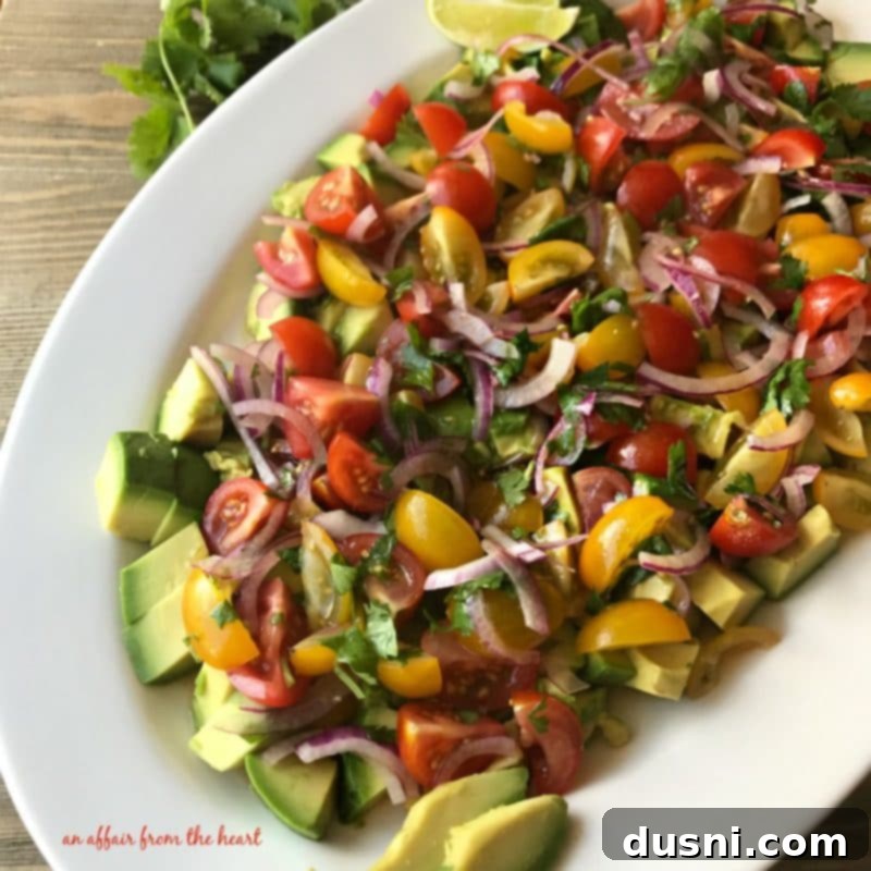 Overhead shot of all fresh ingredients for deconstructed guacamole salad: sliced heirloom tomatoes, chopped red onion, and cilantro on a white background.