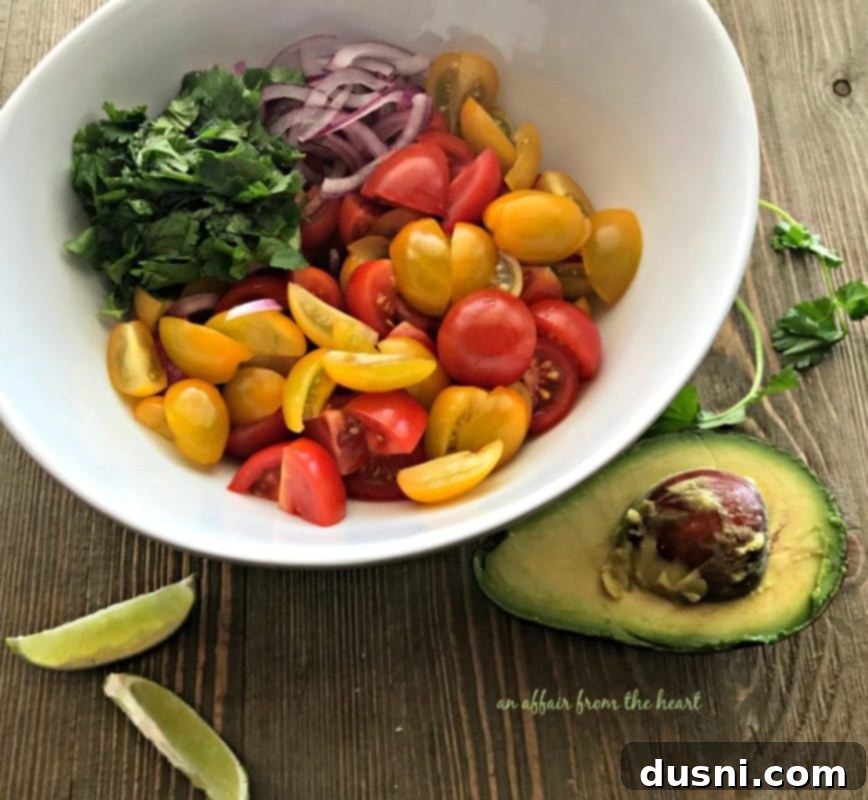 Ingredients for deconstructed guacamole salad being prepped: sliced heirloom tomatoes, red onion, and chopped cilantro on a wooden cutting board.