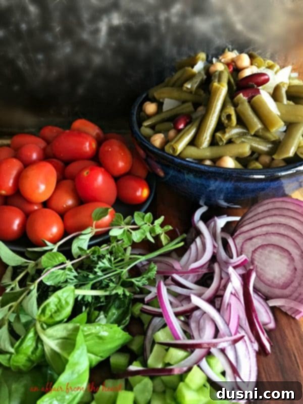 Vibrant Italian Bean Salad 6 Ingredients for Italian Bean Salad laid out: jar of beans, tomatoes, celery, onion, herbs