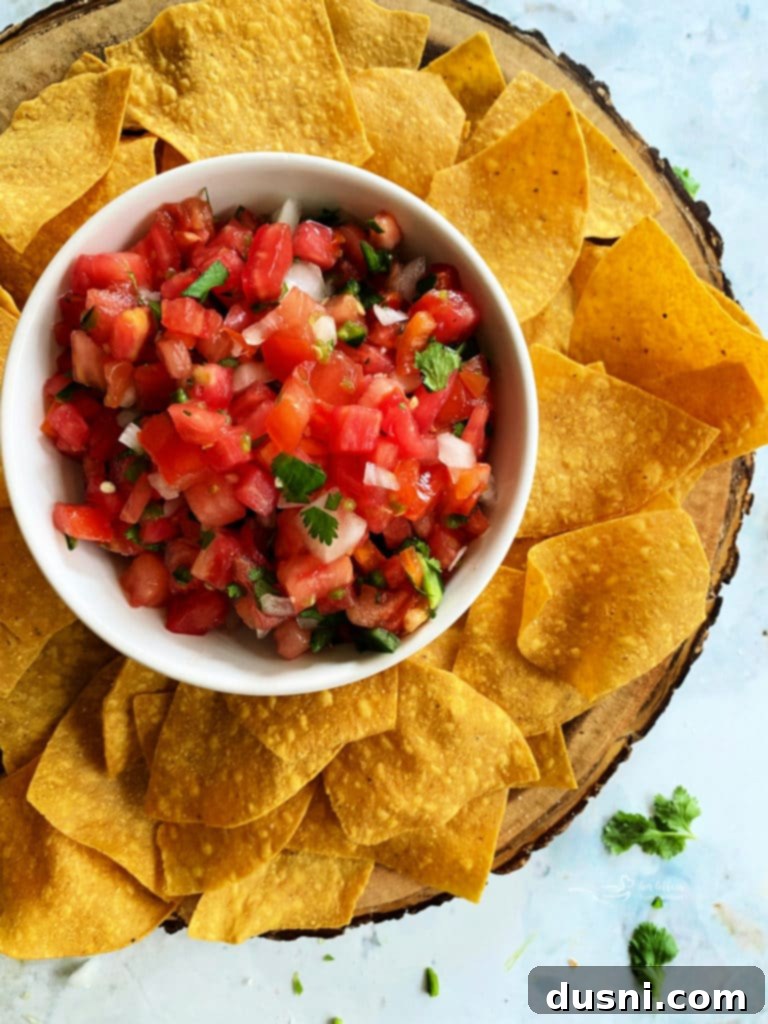 Classic Pico de Gallo in a white bowl surrounded by tortilla chips, ready for dipping.