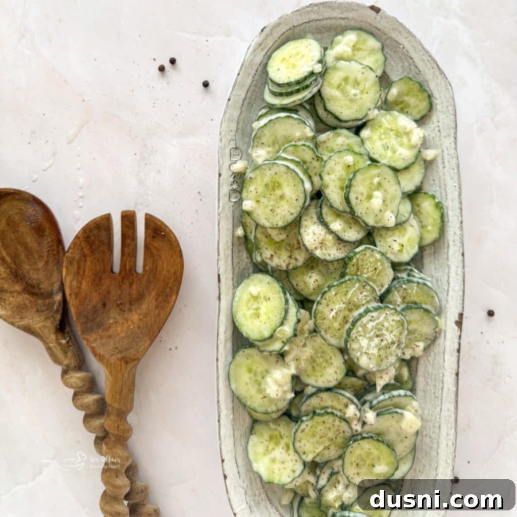 Cucumber Ranch Salad on a white serving dish with wooden salad serving spoons on a light colored table, showcasing fresh ingredients.