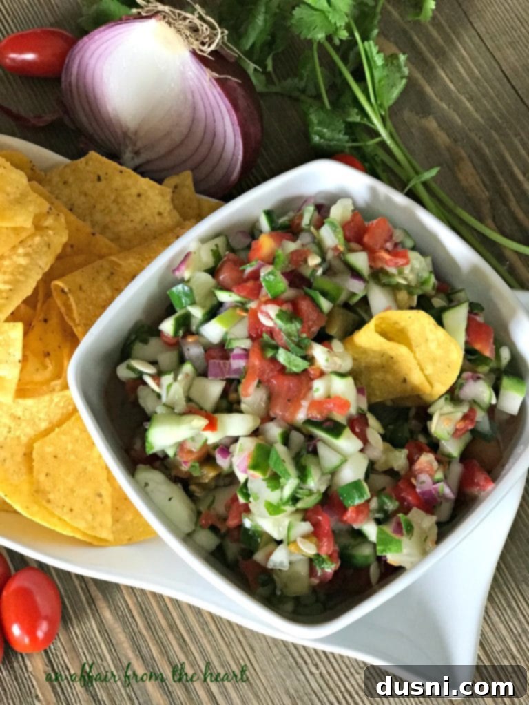 Overhead shot of a bowl of cucumber salsa surrounded by colorful fresh ingredients.