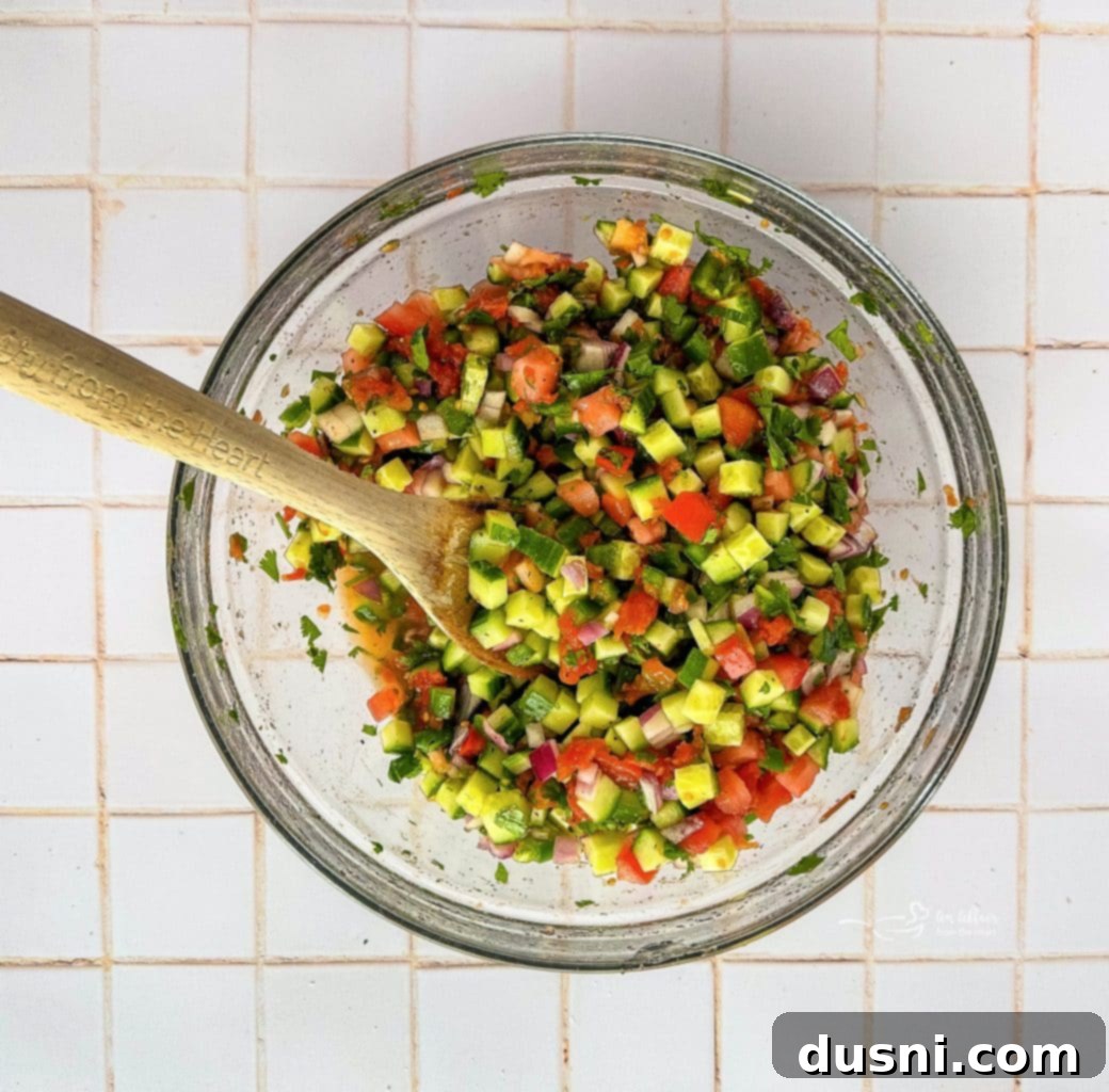Mixing the ingredients for cucumber salsa in a large glass bowl.