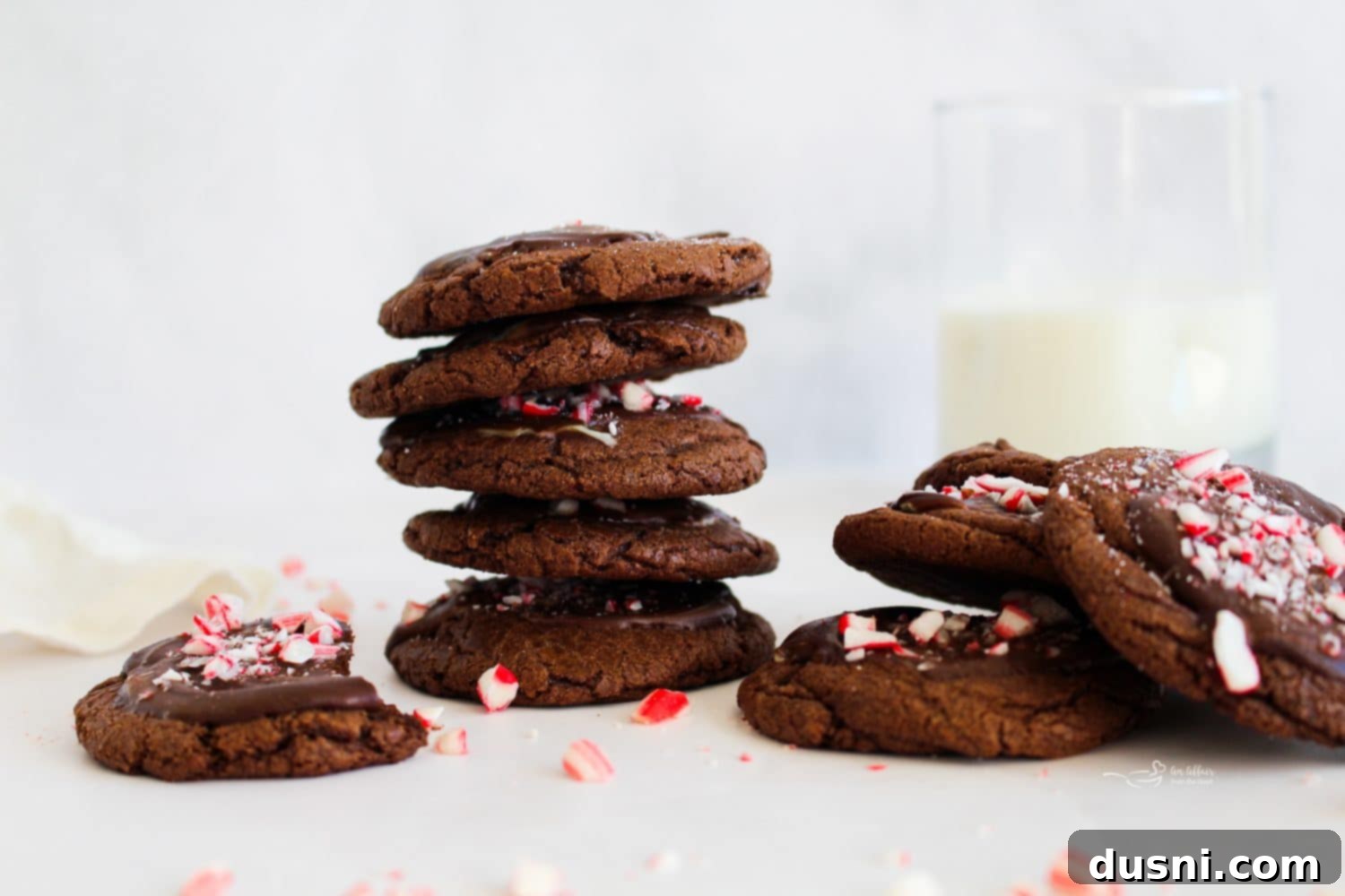 Mint Chocolate Cookie Delights 3 Two hands reaching for a plate of Chocolate Mint Candy Cookies, showcasing their appealing texture and festive toppings.