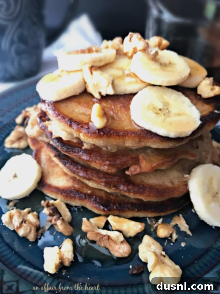 Banana Bread Bliss Stacks 2 Banana Bread Pancakes - A stack of golden brown pancakes topped with banana slices and walnuts, drizzled with maple syrup.