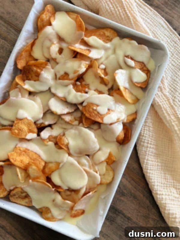 Loaded Reuben Nachos 8 Creamy Swiss cheese sauce being poured generously over a bed of potato chips on a baking sheet
