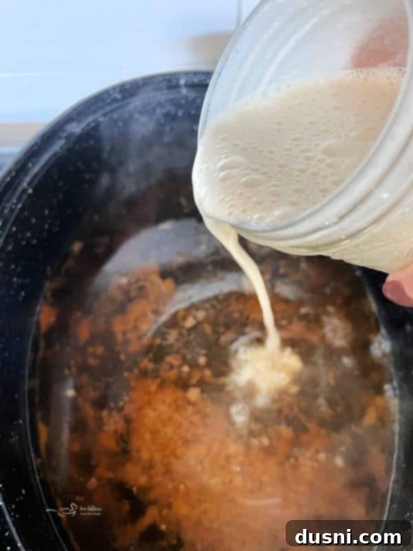Milk and flour slurry being poured into bubbling pork drippings in a roasting pan on the stovetop.