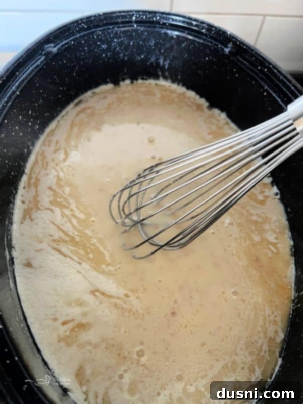 A whisk stirring homemade gravy in a roasting pan on the stovetop, showing the thickening process.