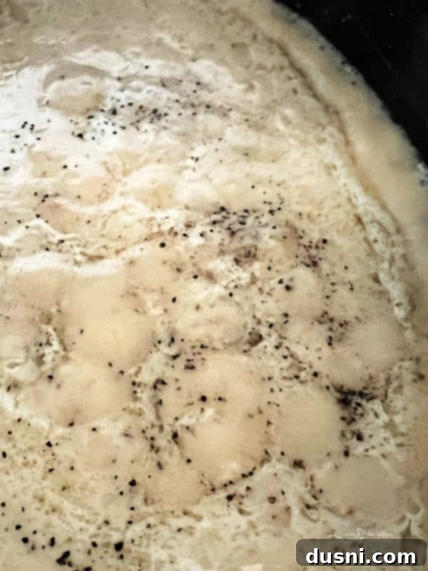 A close-up shot of a perfectly thickened, smooth homemade pork gravy in a roasting pan.