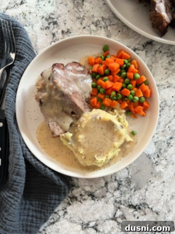 A generous serving of tender pork roast and mashed potatoes, drenched in savory homemade gravy, ready to be enjoyed.
