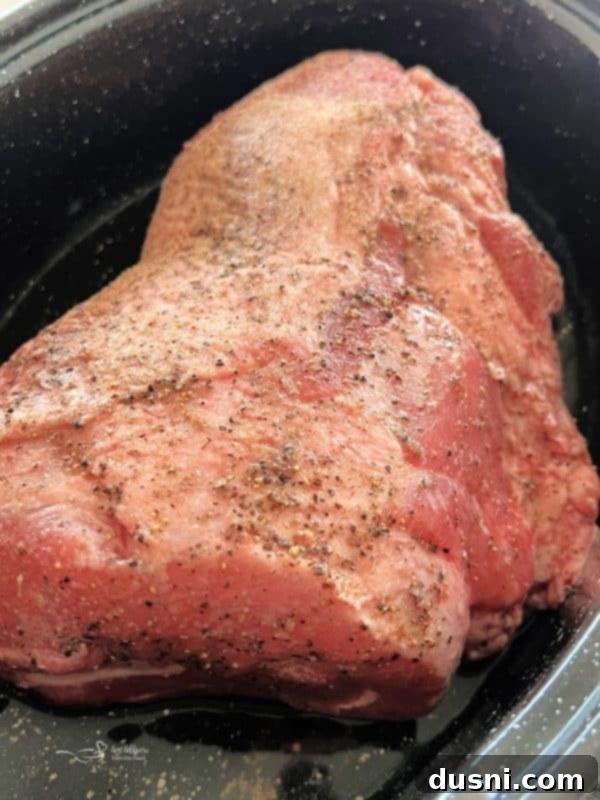 Close up of a fork pulling a piece of tender pork roast from the main dish, emphasizing its perfect texture.