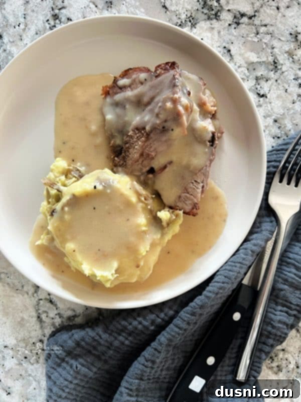 A beautifully presented, rustic platter of roasted pork and mashed potatoes, generously topped with gravy, ready for a comforting meal.