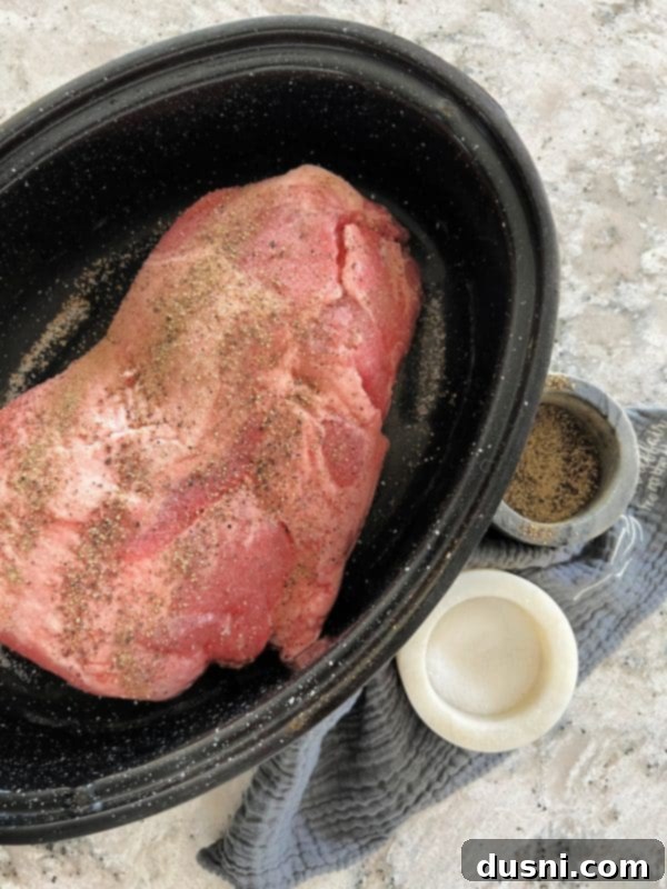 Pork shoulder roast seasoned with salt and pepper in a roasting pan, ready for the oven.