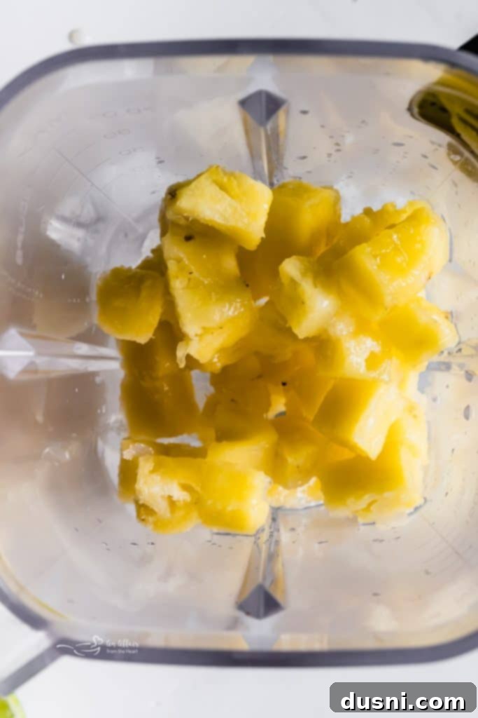 Blender with pineapple chunks, lime, and other margarita ingredients ready to be blended.