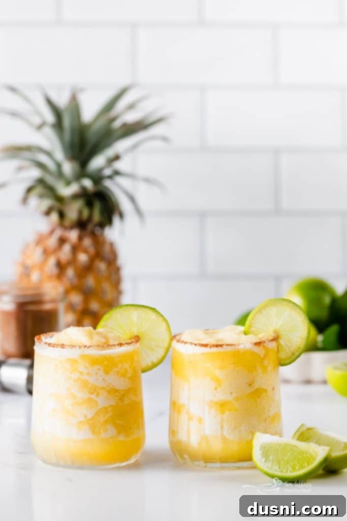Close-up of a Frozen Pineapple Margarita in a glass with a lime wedge and a spicy rim, ready to drink.
