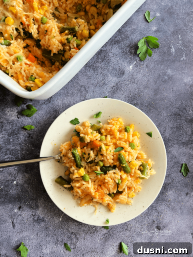 Dorothy's Golden Cheesy Vegetable Rice Bake 2 A serving of Cheesy Vegetable Rice Bake, with visible rice, cheese, and vegetables on a white plate with a fork.