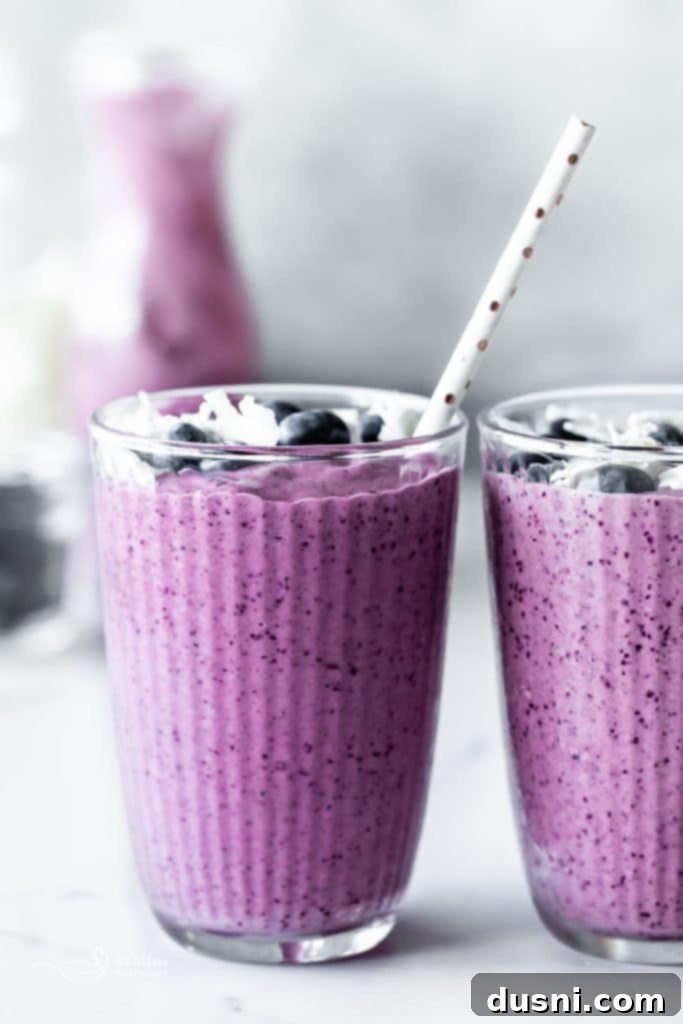 Vibrant Blueberry Pineapple Refresher 2 A vibrant Blueberry Pineapple Smoothie in a glass with fresh blueberries and pineapple chunks around it.