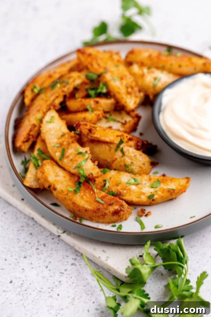 Close-up of crispy roasted Parmesan garlic potato wedges in a white bowl with fresh parsley garnish.