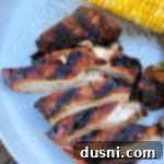 Sliced Sweet & Smoky Chicken and an ear of corn on a white plate.