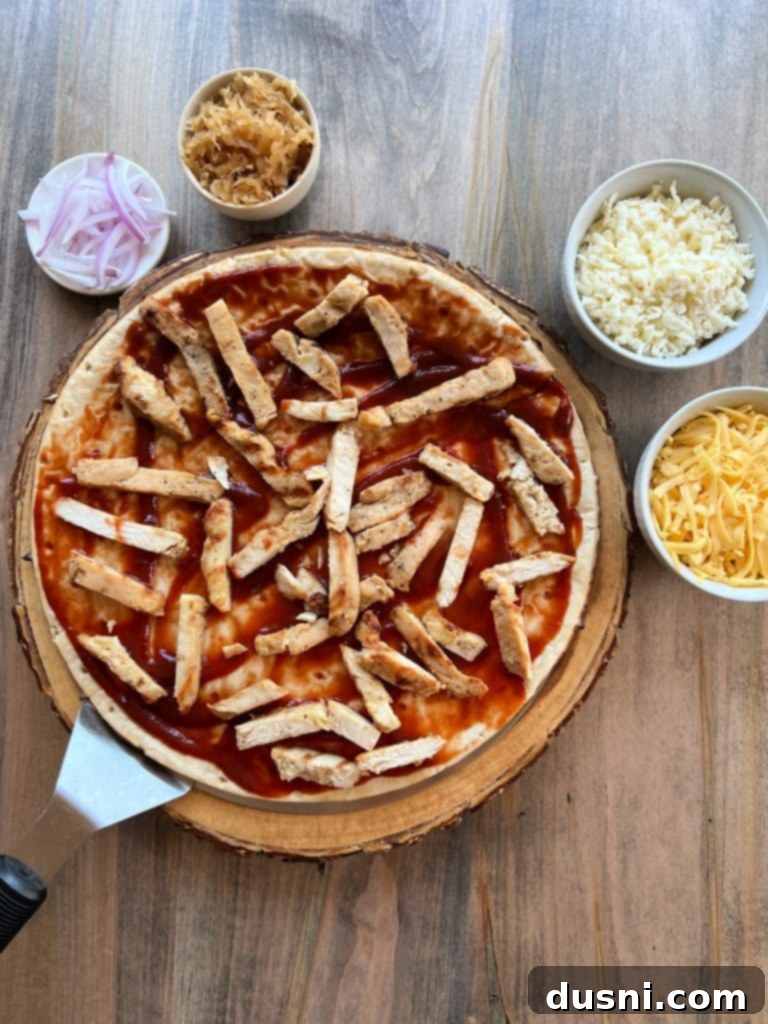 Step 2: Layering grilled chicken and thinly sliced red onion on the sauced pizza crust.