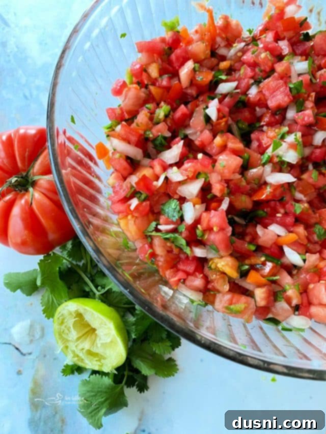 Irresistible Dips for Every Occasion 25 Overhead view of fresh Pico de Gallo in a clear bowl, highlighting the vibrant colors of tomatoes, onions, and cilantro.