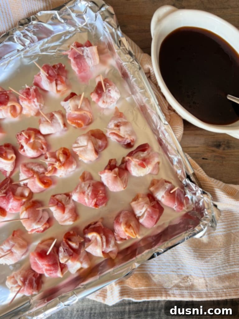 Hands wrapping a slice of bacon around a water chestnut, preparing it for the oven.